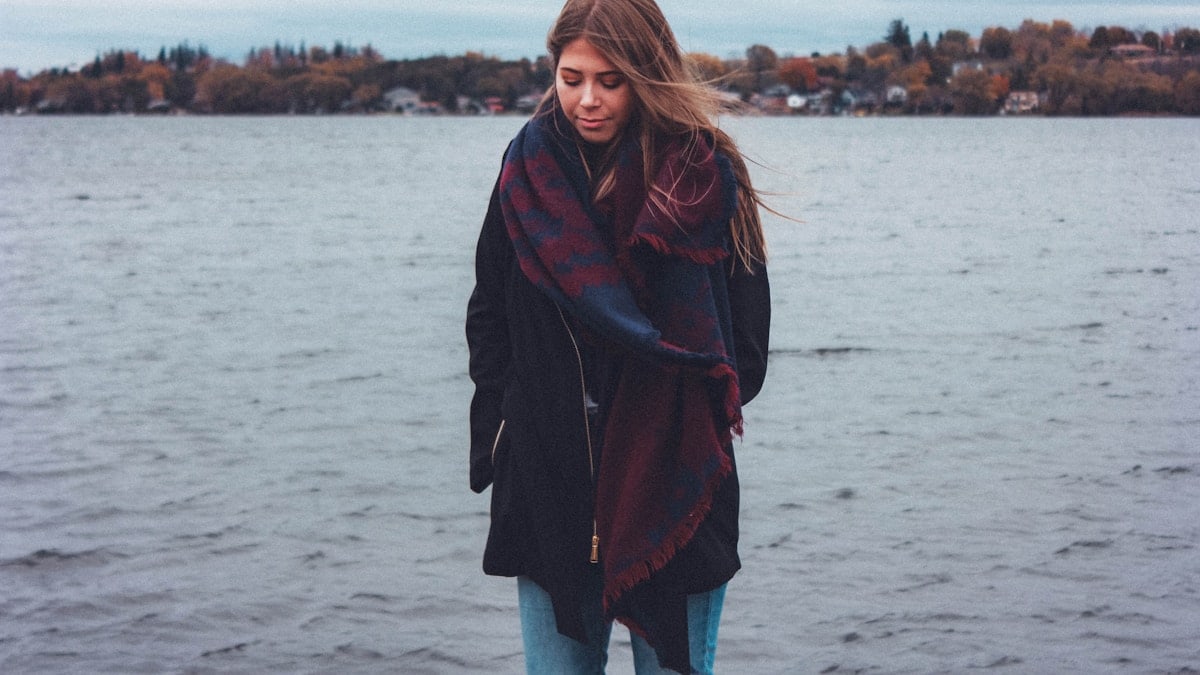 woman wearing red coat standing near body of water